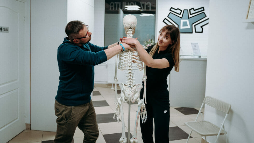 Mężczyzna i kobieta stojący obok szkieletu w gabinecie fizjoterapii.